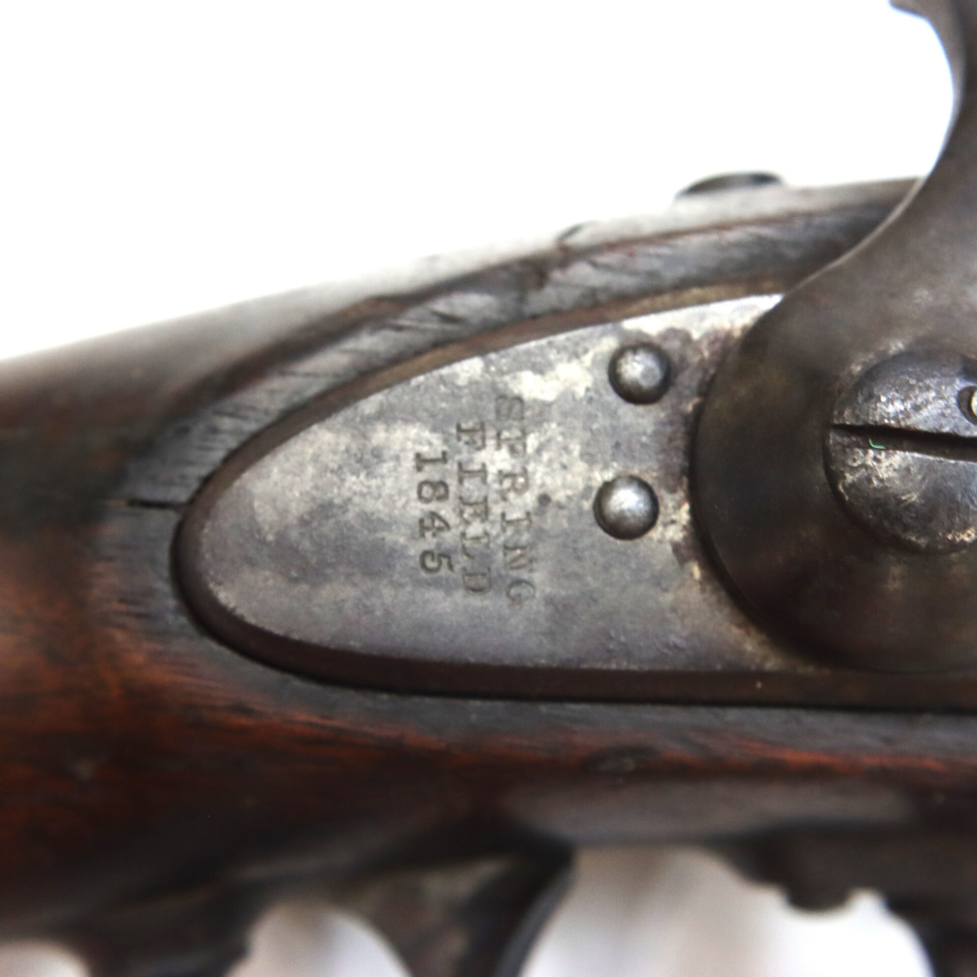 Metal lock plate of a Model 1842 .69 Caliber Springfield Smoothbore Musket, engraved with “SPRING FIELD 1845” next to a hammer mechanism and wooden stock.