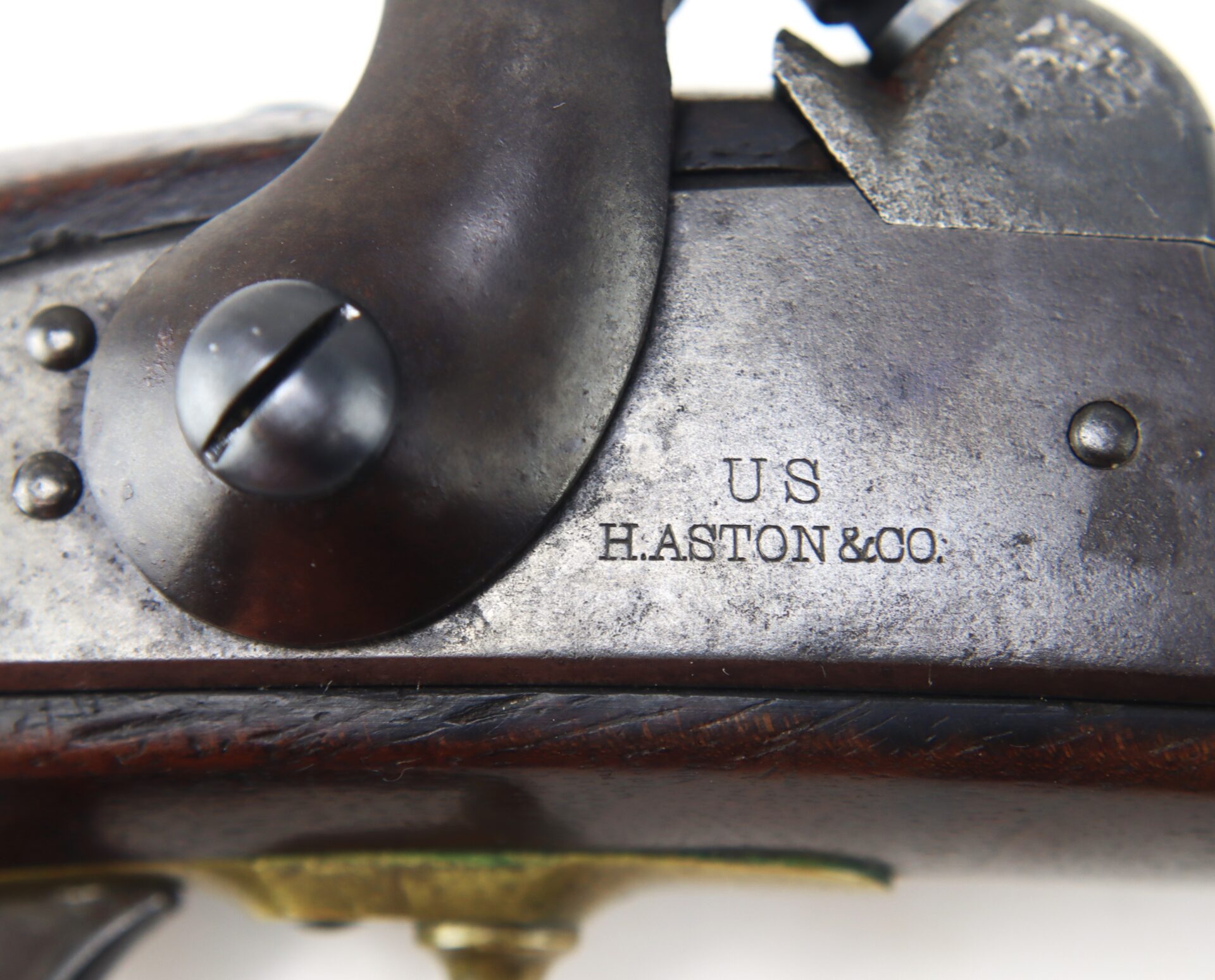 Close-up of a metal firearm part stamped with “U.S H.ASTON & CO.” The metal is attached to a wooden stock and shows signs of age.
