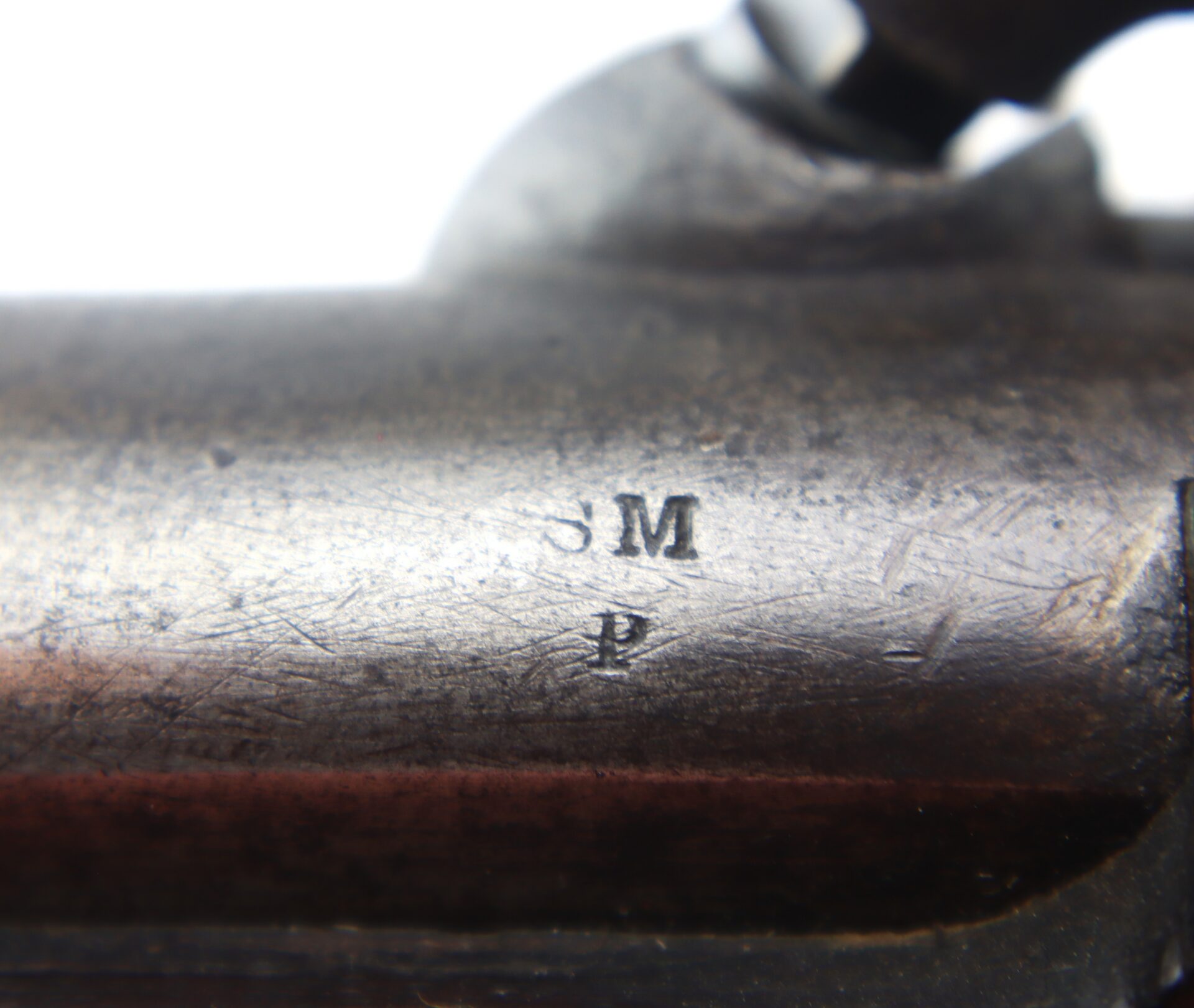 Close-up of a metal surface with visible scratches and engraved letters “S M” above “P.”.