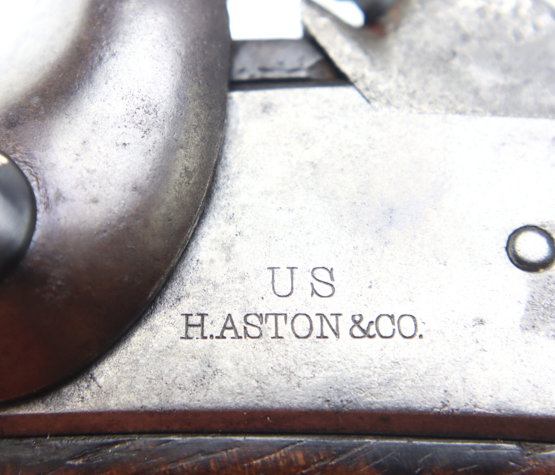 Close-up of a metal surface engraved with “U S” and “H. ASTON & CO.” near a mechanical component, possibly part of a vintage firearm.