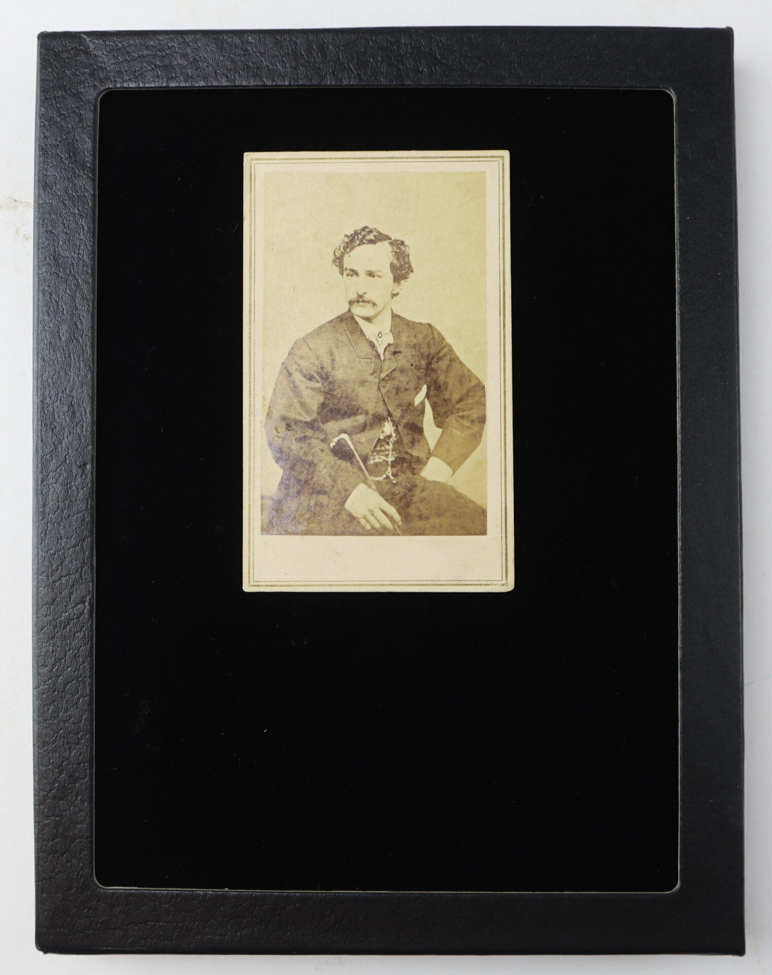 Sepia-toned portrait photograph of a seated man with a mustache, dressed in formal attire, displayed in a black rectangular frame.