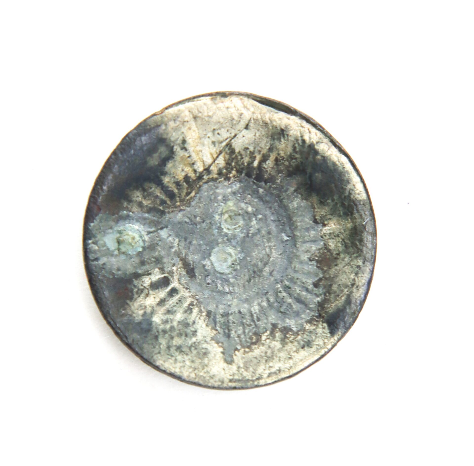 A close-up of a weathered, tarnished metallic coin or token with indistinct markings and signs of corrosion.