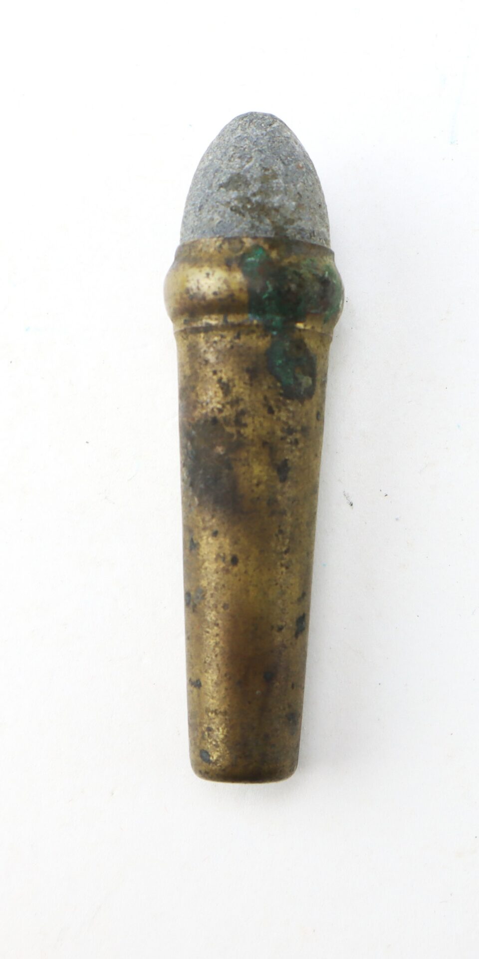A corroded, old bullet with a lead tip and brass casing, standing upright on a white background.