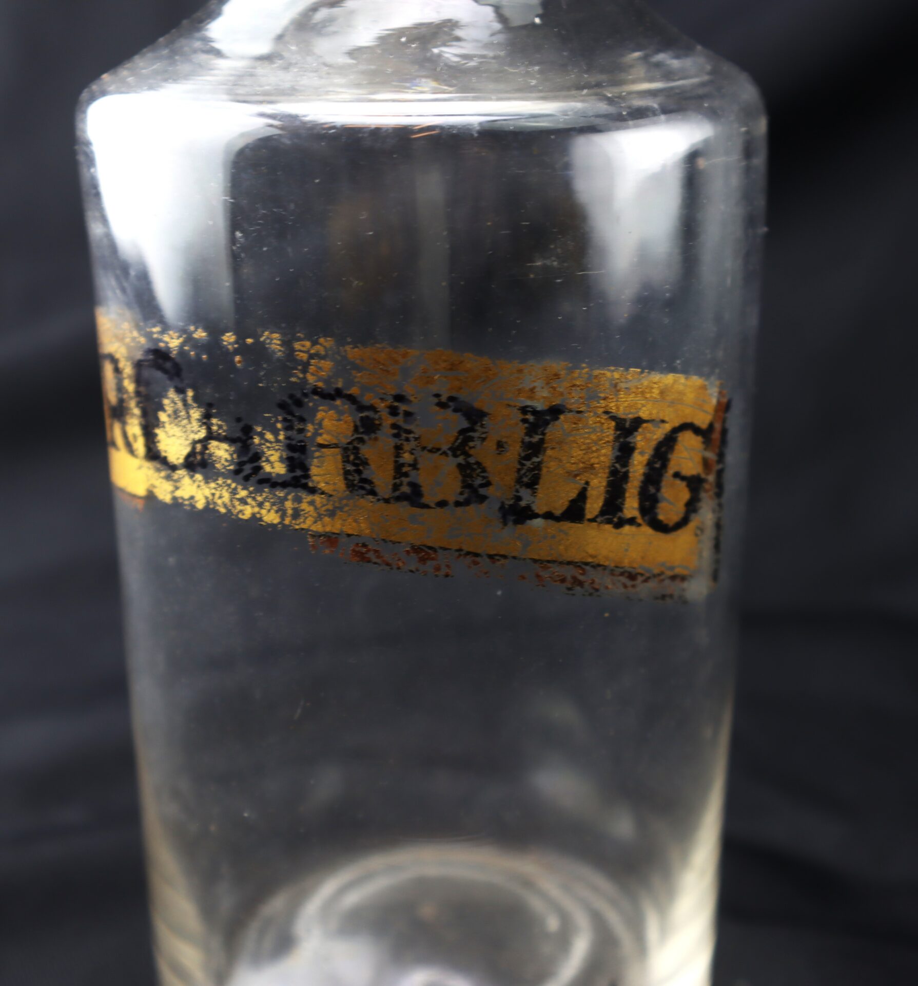 A clear glass bottle with a gold and black faded label that partially reads “COURBLI.” The background is black.