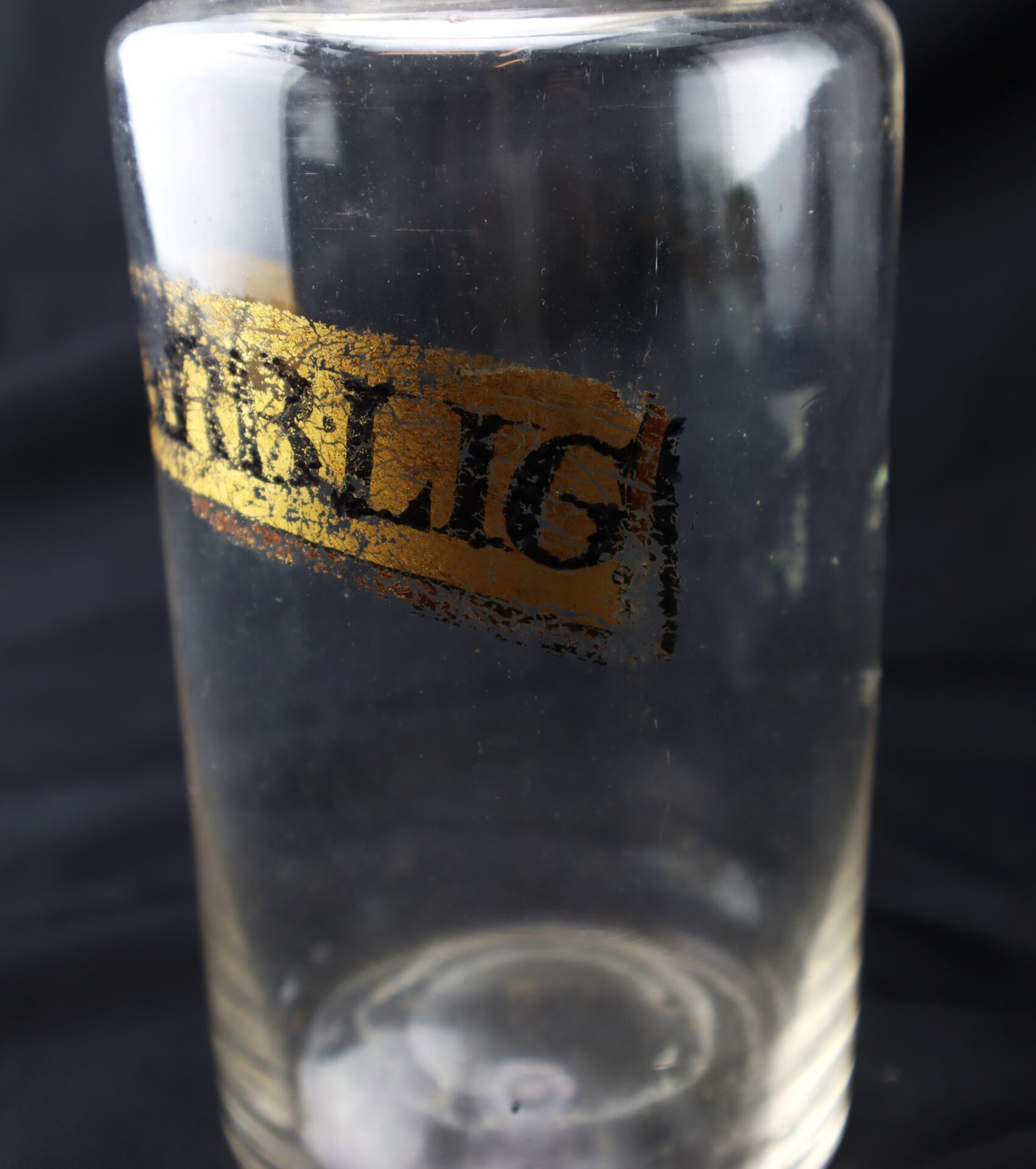 A clear glass jar with a partially peeled gold and black label that reads “RLIG” against a black background.