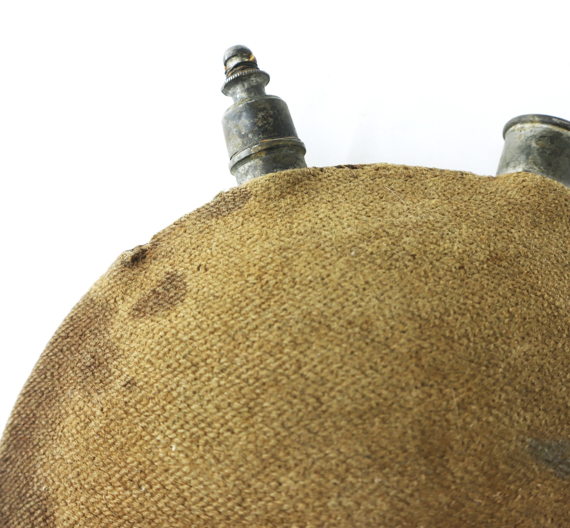 Close-up of the top part of a vintage canteen with a textured fabric cover and two metal spouts against a white background.