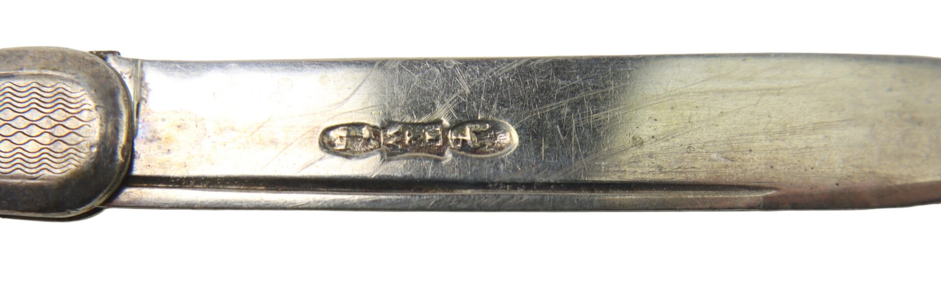 Close-up of a metal pocket knife blade with visible engravings and textured handle detail on the left side.