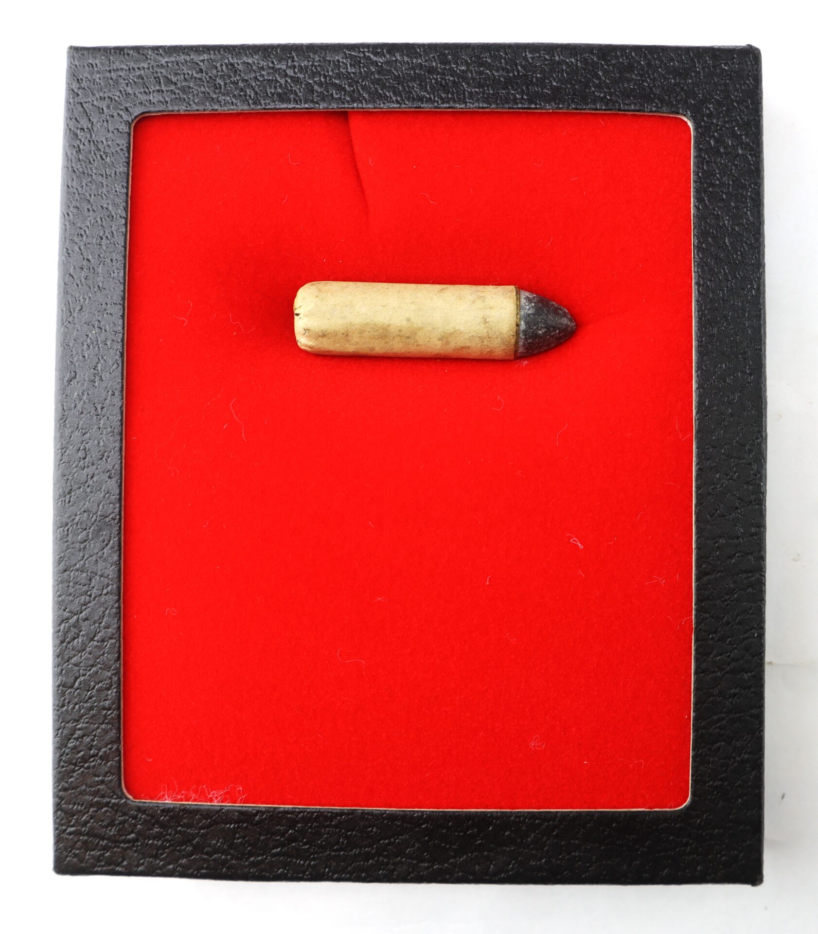 A single bullet displayed in a black square case with a red velvet background.