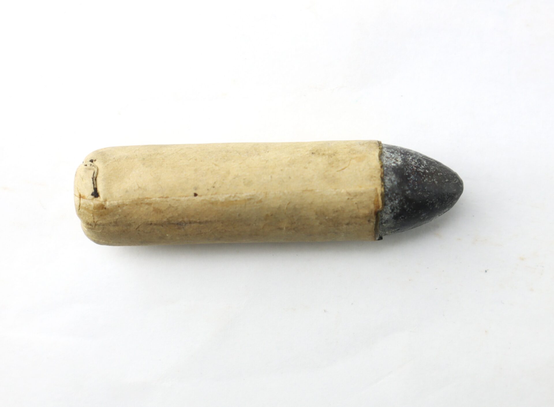 A paper cartridge with a visible lead bullet tip sits on a white surface.
