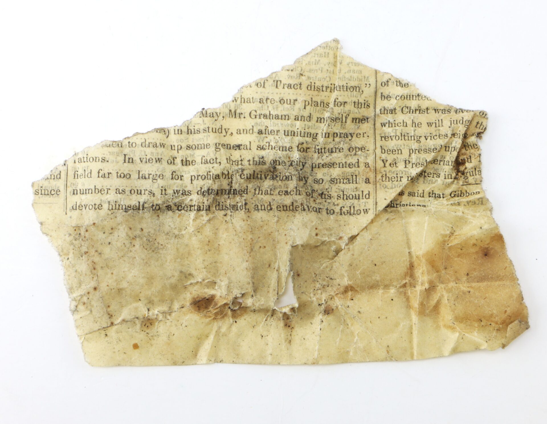 A torn, dirty piece of old yellowed paper with faded, partially readable printed text on its surface.