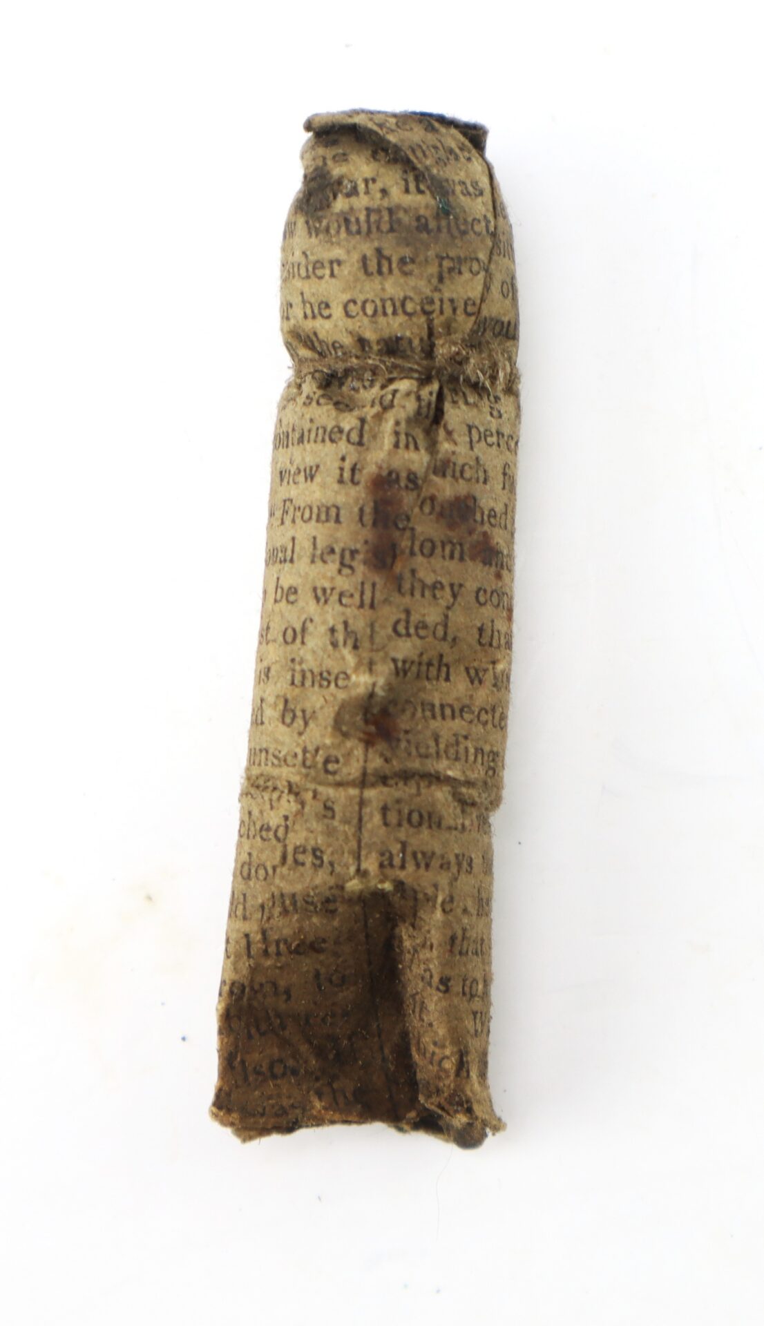 A small object wrapped in aged, printed paper with visible text, shaped roughly like a cylindrical figure, displayed against a white background.