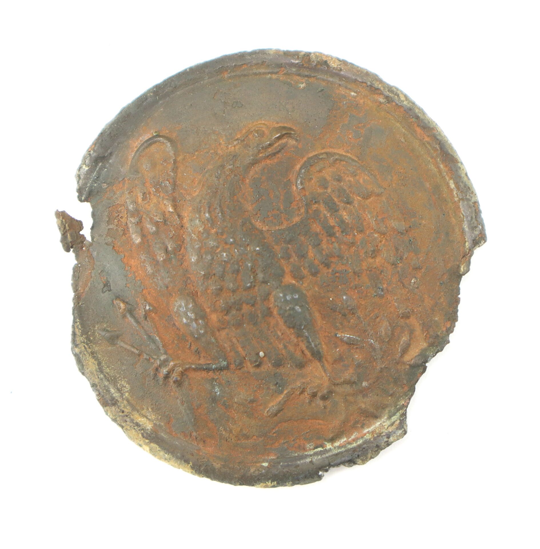 Round, rusted metal object with an embossed eagle design, partially damaged at the edge.
