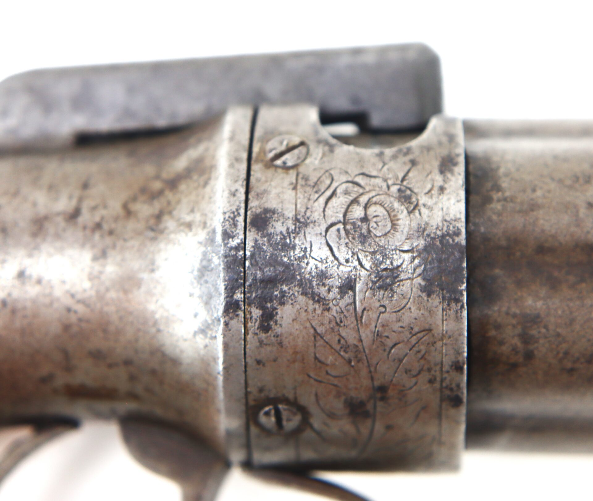 Close-up of an old metal firearm with visible engraving of a rose and leaves near two screws.