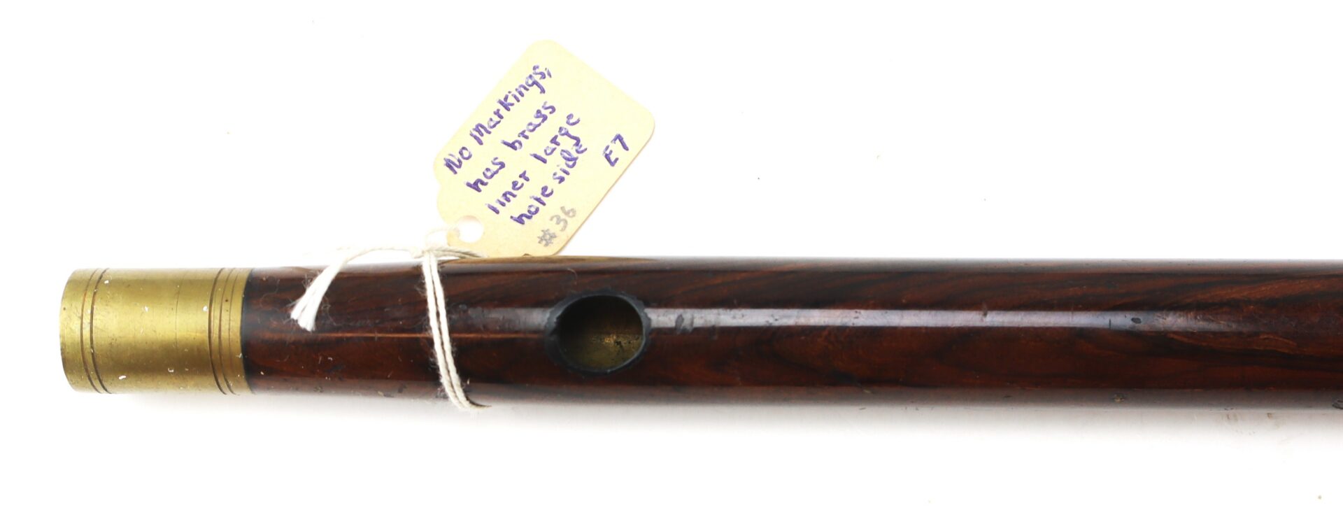Close-up of a wooden flute with a brass end and a handwritten tag attached by string, displaying a message and numbers.
