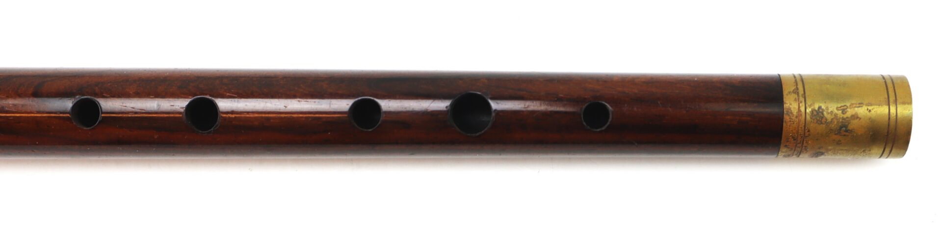 A close-up of a wooden flute with six finger holes and a brass end cap on a white background.