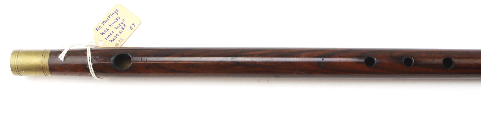 A wooden flute with brass trim, four finger holes, and a small label attached with a string near the end.