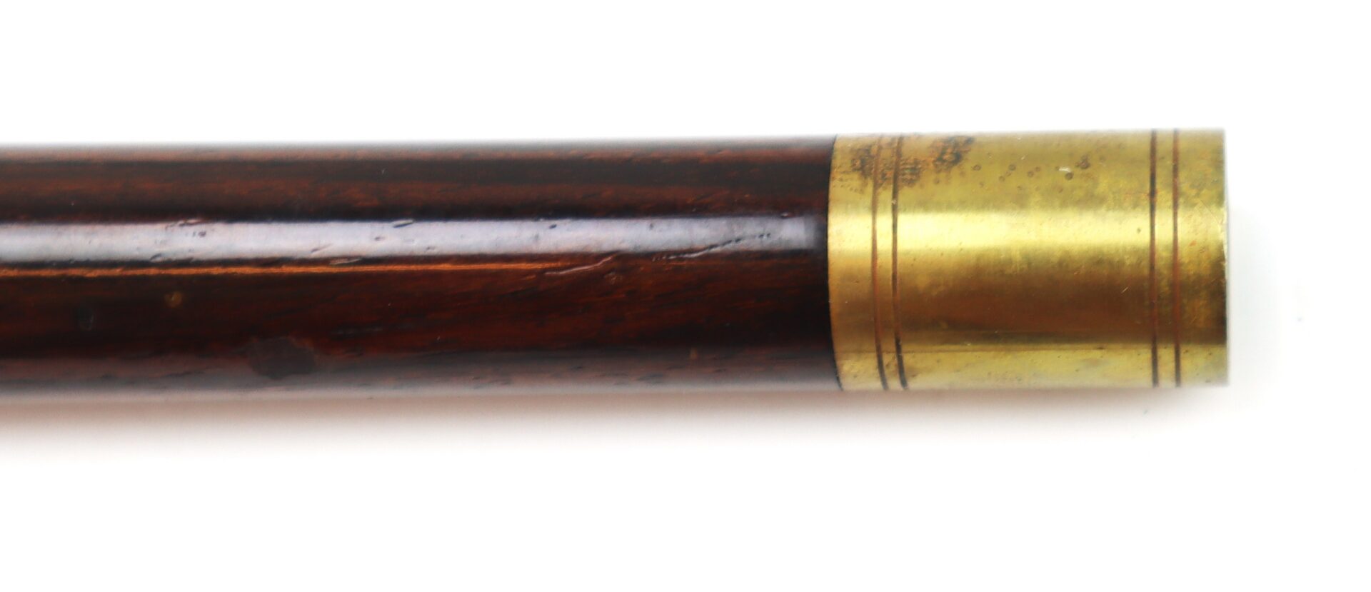A close-up of a wooden rod or staff with a polished brass band near one end, set against a white background.