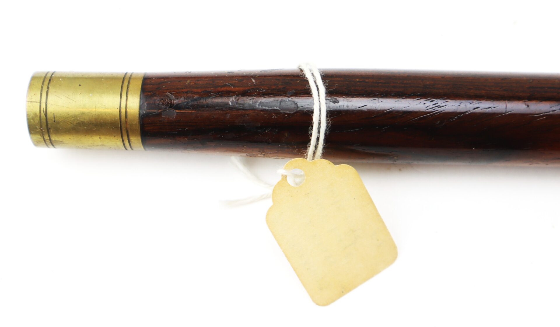 Close-up of a wooden walking stick or cane with a brass collar and a blank, scalloped-edge tag tied around it with white string.