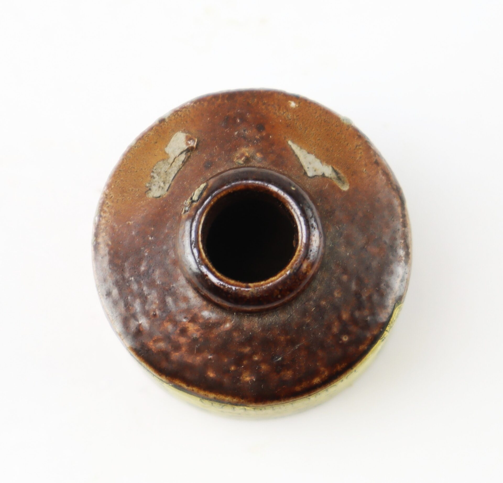 Top-down view of a small, round brown ceramic jar with a narrow opening.