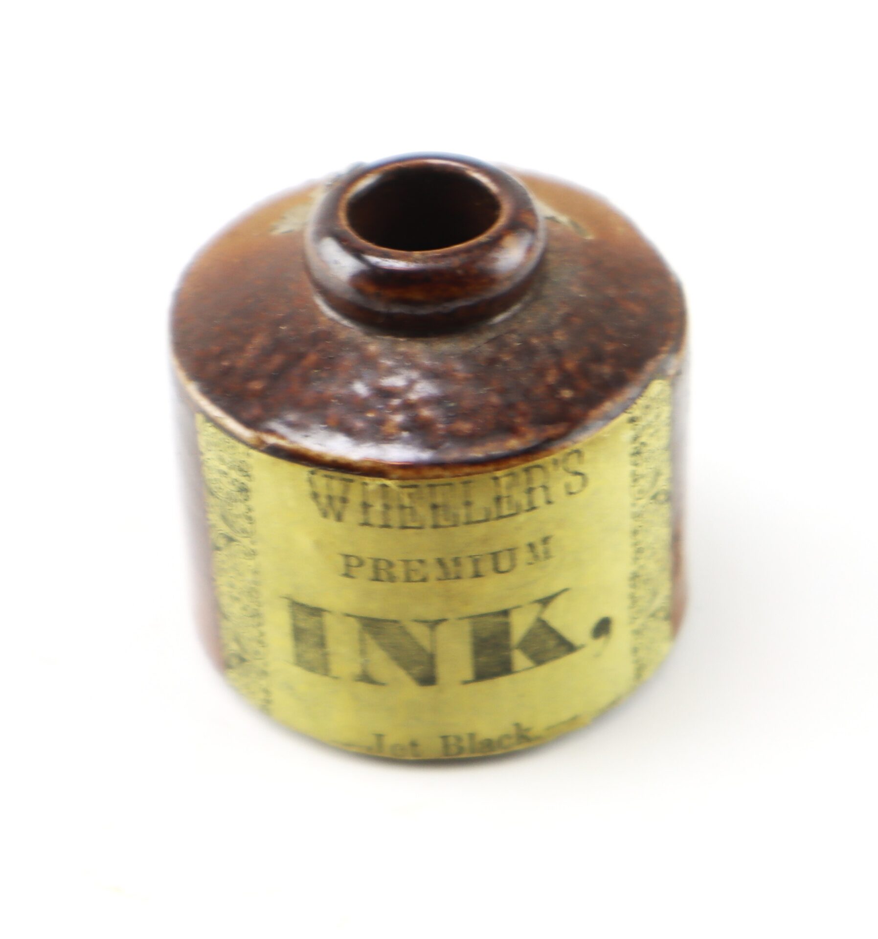 Antique brown stoneware ink bottle with a yellow label that reads “Wheeler’s Premium Ink, Jet Black.”.