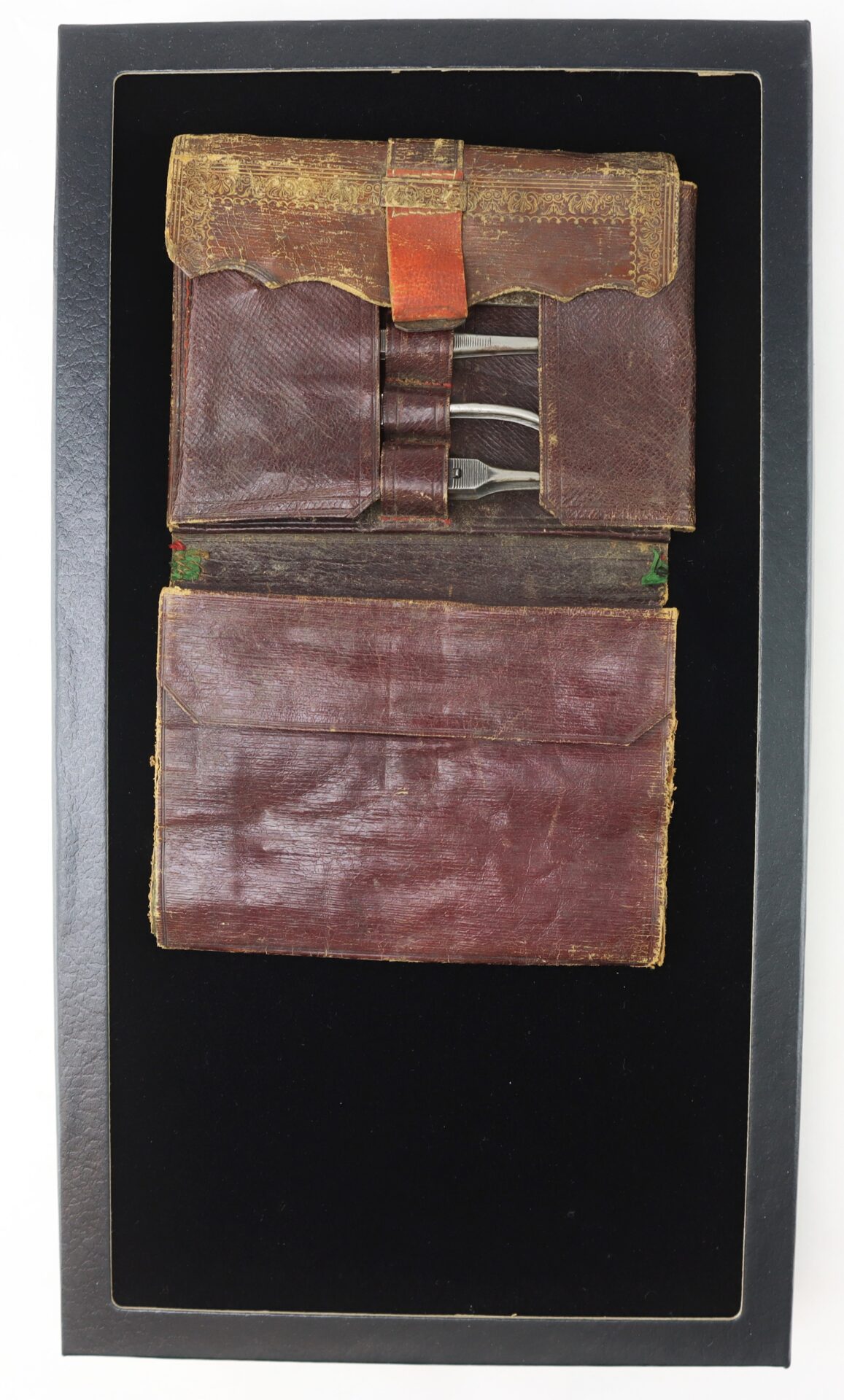 A vintage brown leather travel kit containing small metal grooming tools, displayed in a black presentation box.