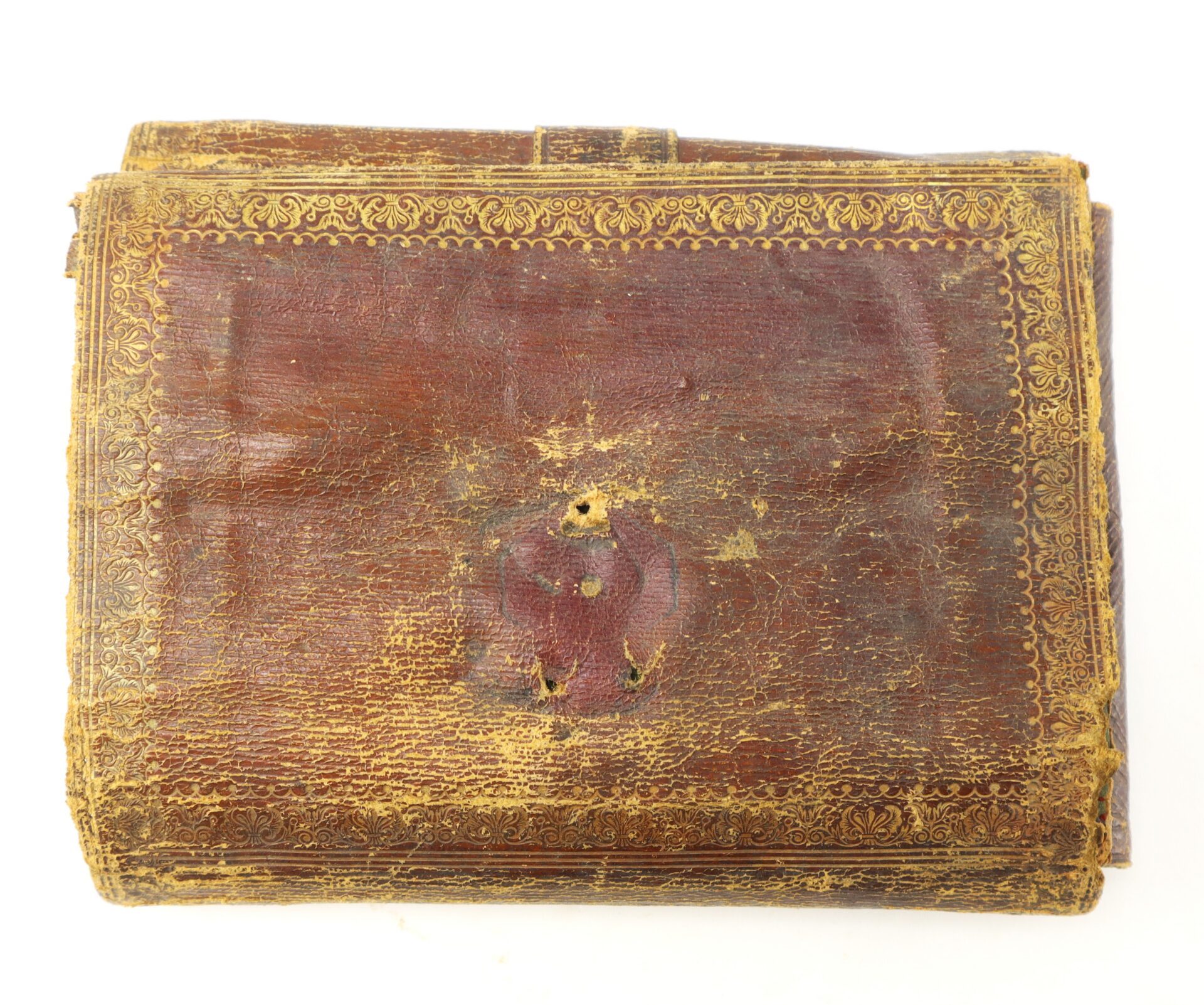 A rectangular, worn brown leather book with decorative gold-tooled borders and a faded circular emblem in the center.