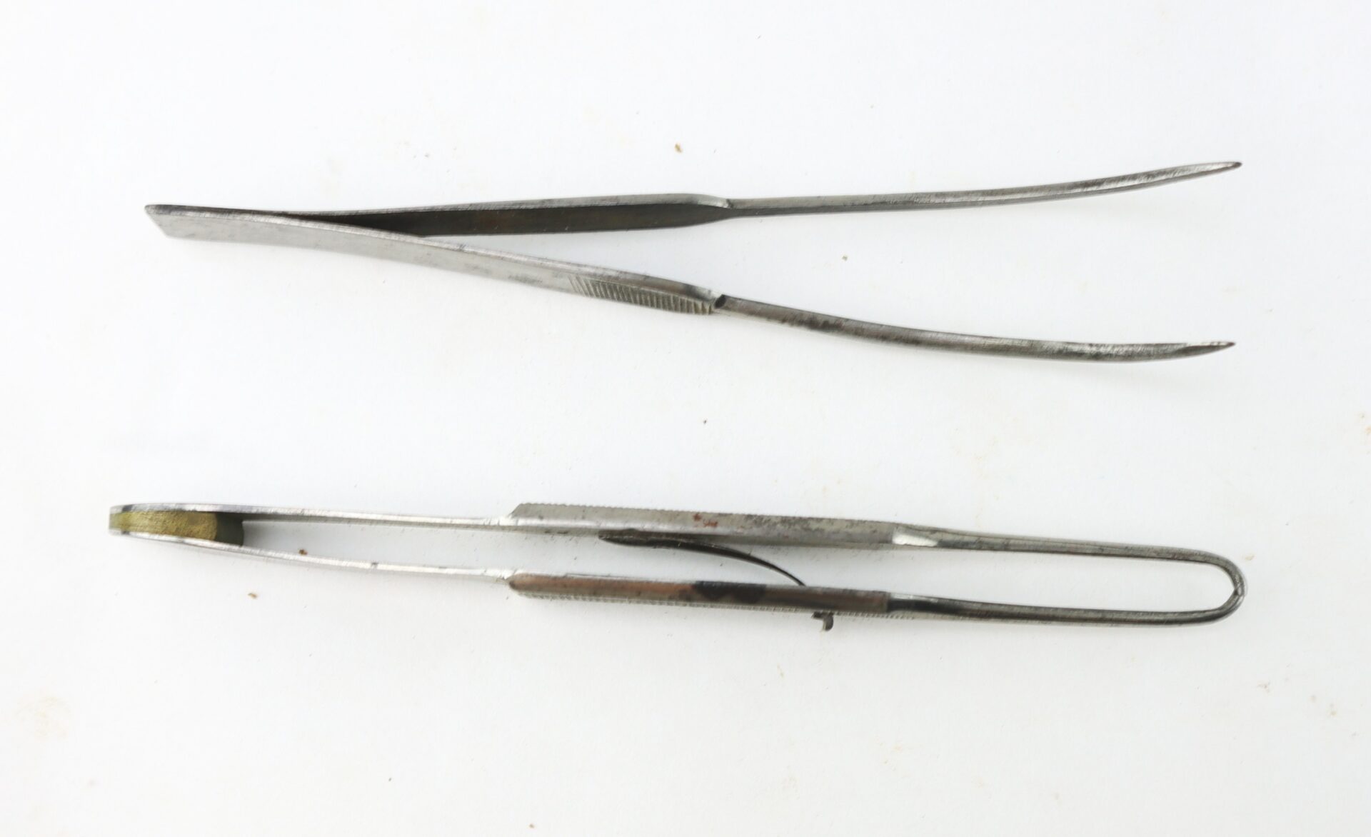Two pairs of metal tweezers on a white background.