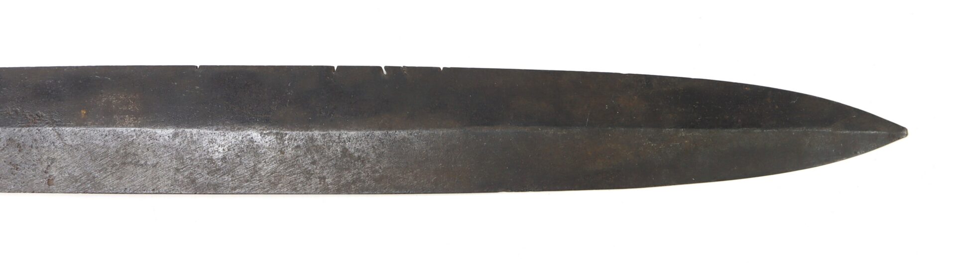 The pointed, weathered metal blade of a sword or dagger with visible nicks along the edge.