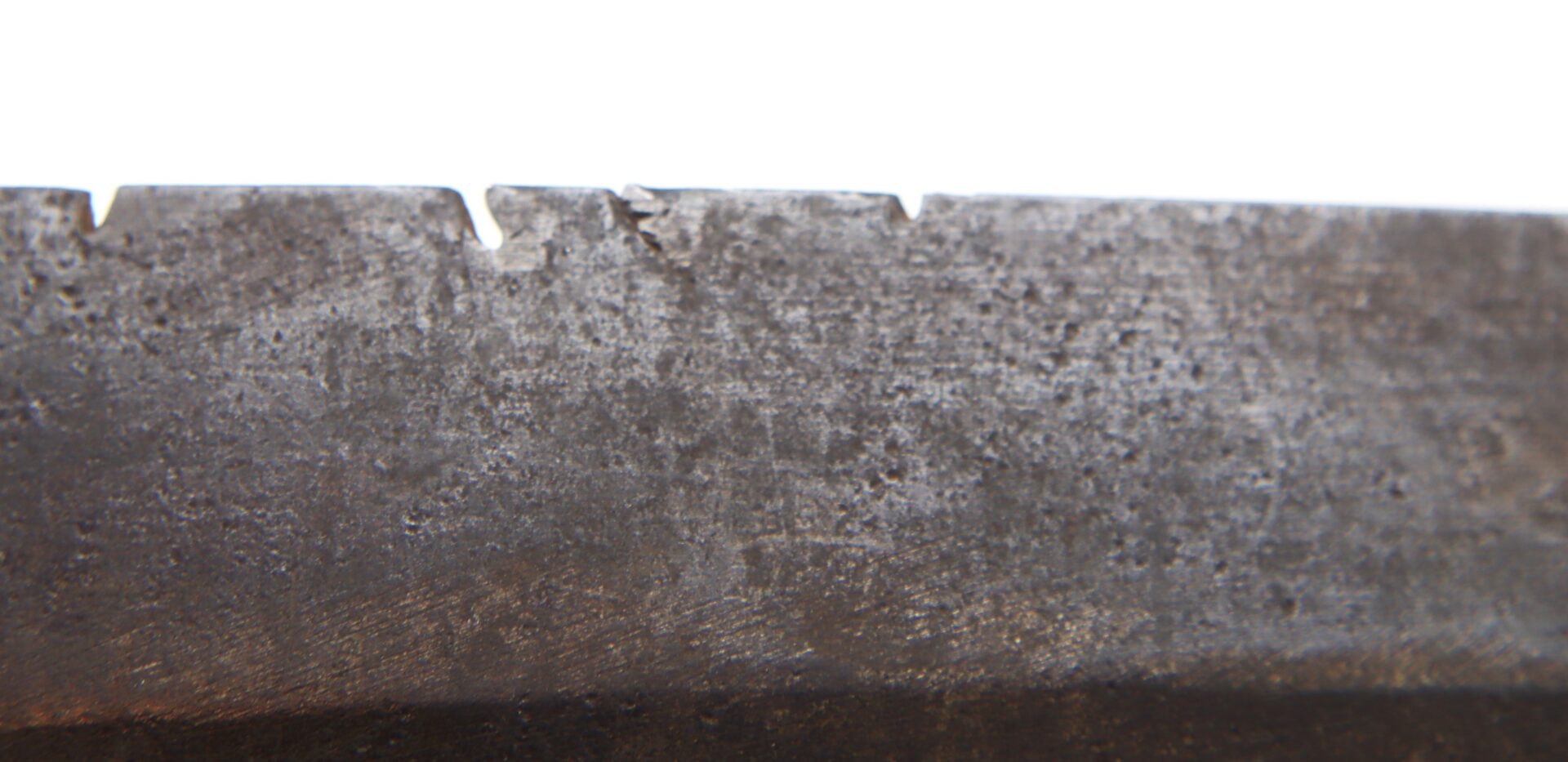 Close-up of a dull, textured metal blade edge with multiple small notches.